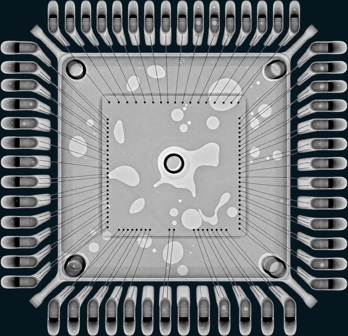 X-ray of a quad flat package showing bond wires and large irregular voids in the die attach layer